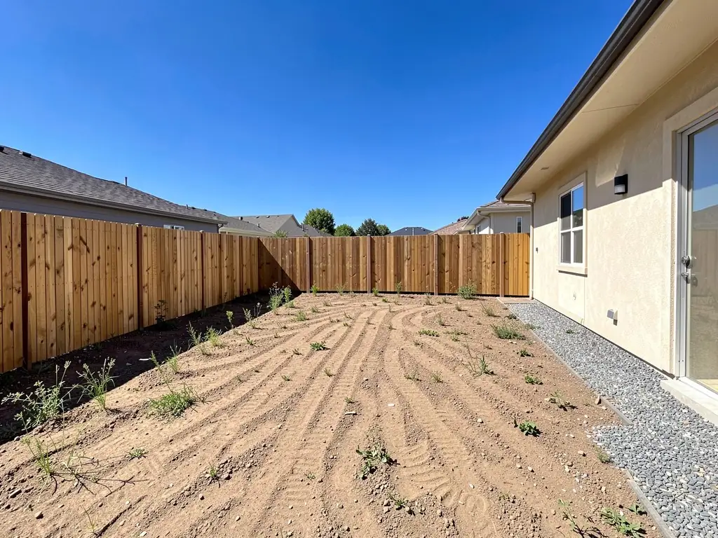 Before: Bare, raked dirt side yard of a new stucco home before and after an AI landscape design in the Modern style, with a lawn, corten-edged beds of grasses and boxwood, two young trees and a concrete path